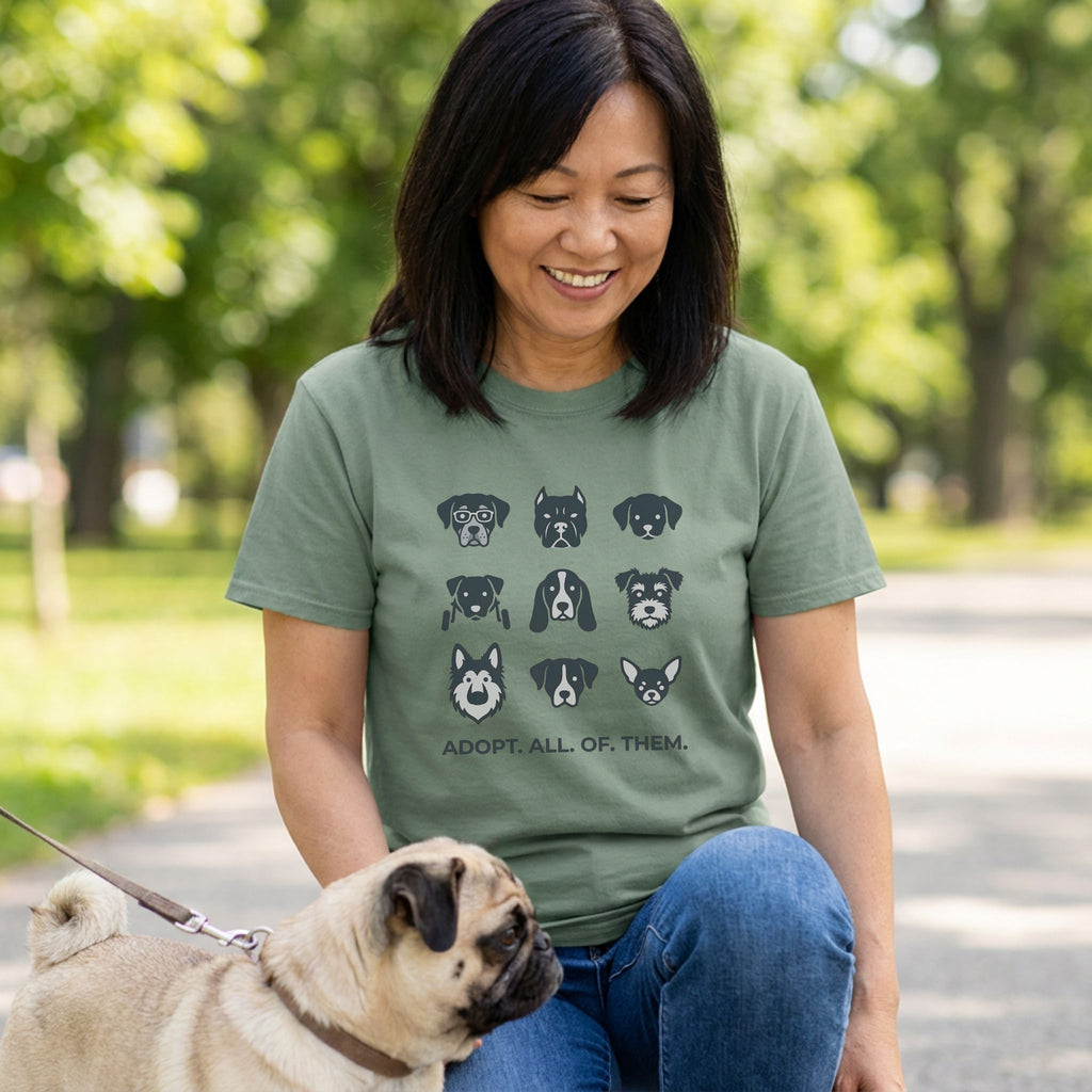 Woman in an olive green "Adopt All of Them" t-shirt with dog faces, petting a pug outdoors.