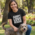Woman in black "ADOPT LOVE RESCUE" t-shirt petting a scruffy dog in a park.