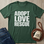Forest green Gildan Softstyle® t-shirt with "ADOPT LOVE RESCUE" in white, next to jeans and dog treats.