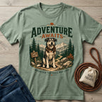 Sage green crewneck t-shirt featuring a graphic of a dog holding a leash on a mountain trail with Adventure Awaits text.