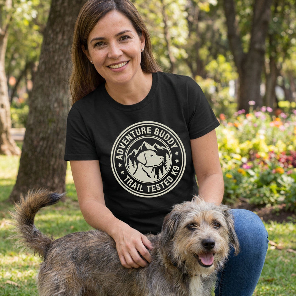 Woman in black "Adventure Buddy Trail Tested K9" tee petting a rescue dog outdoors.