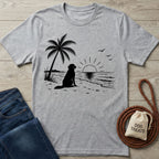 Grey crewneck t-shirt featuring a black graphic of a dog sitting on a beach under a palm tree at sunset.