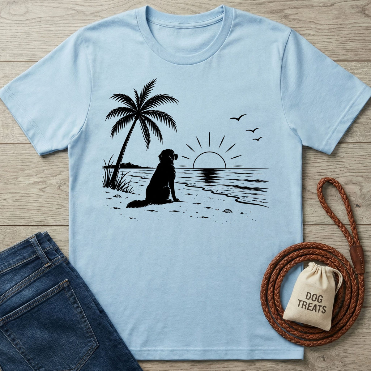 Light blue crew neck t-shirt featuring a black silhouette of a dog sitting on a beach under a palm tree at sunset.