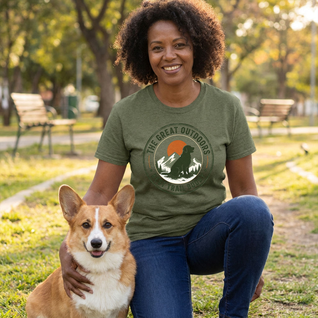 Woman wearing an olive green crewneck t-shirt with a hiking dog graphic, kneeling outdoors with a corgi.