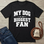 Black crewneck t-shirt featuring white text that reads My Dog Is My Biggest Fan, displayed with jeans and a treat bag.