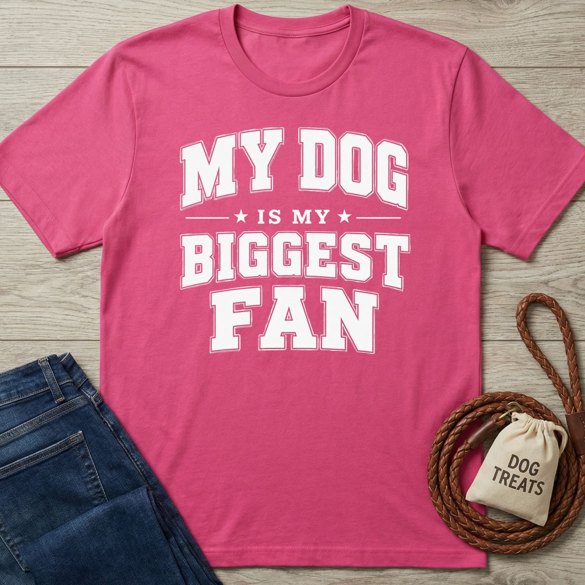 Hot pink crewneck t-shirt with white collegiate-style text reading My Dog Is My Biggest Fan on a wooden background.