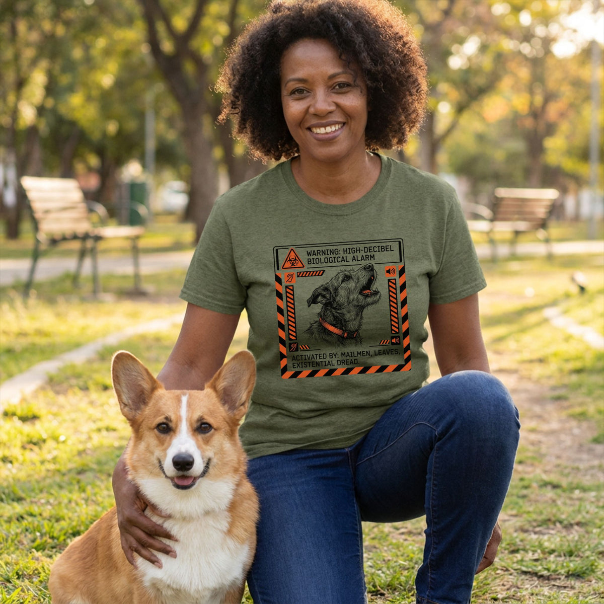Woman in an olive green "Biological Alarm" t-shirt with a barking dog graphic, kneeling with a corgi.