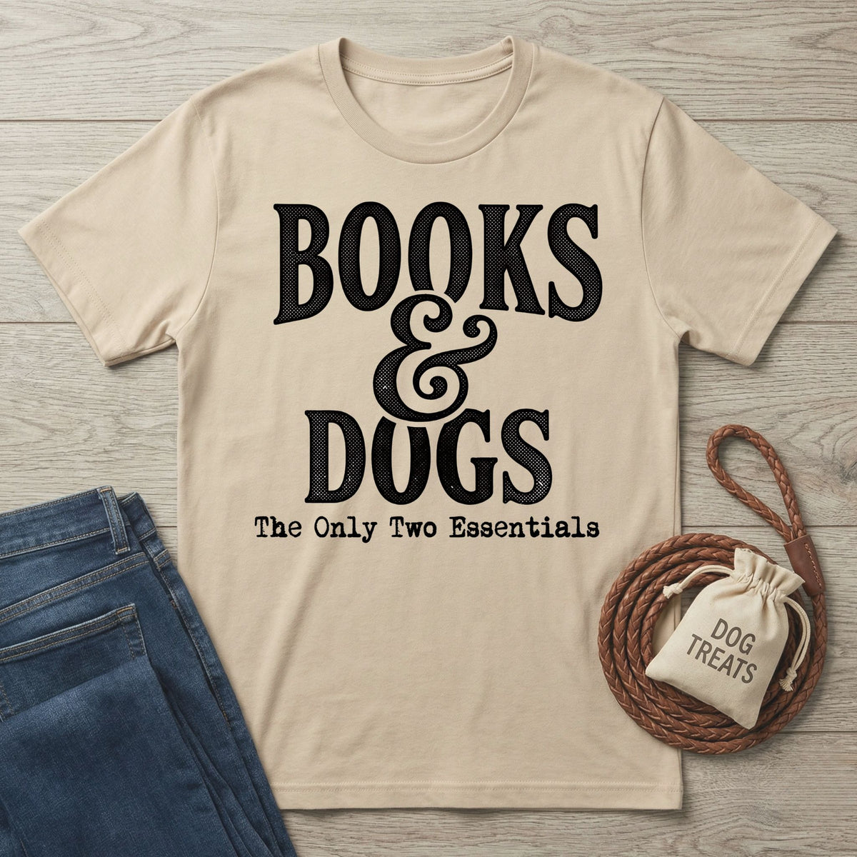Beige crewneck T-shirt with black Books & Dogs graphic text, displayed with blue jeans, a dog leash, and a treat bag.