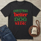 Black crewneck T-shirt with red and green Christmas text, featuring paw prints and a dog treats pouch on a wooden surface.