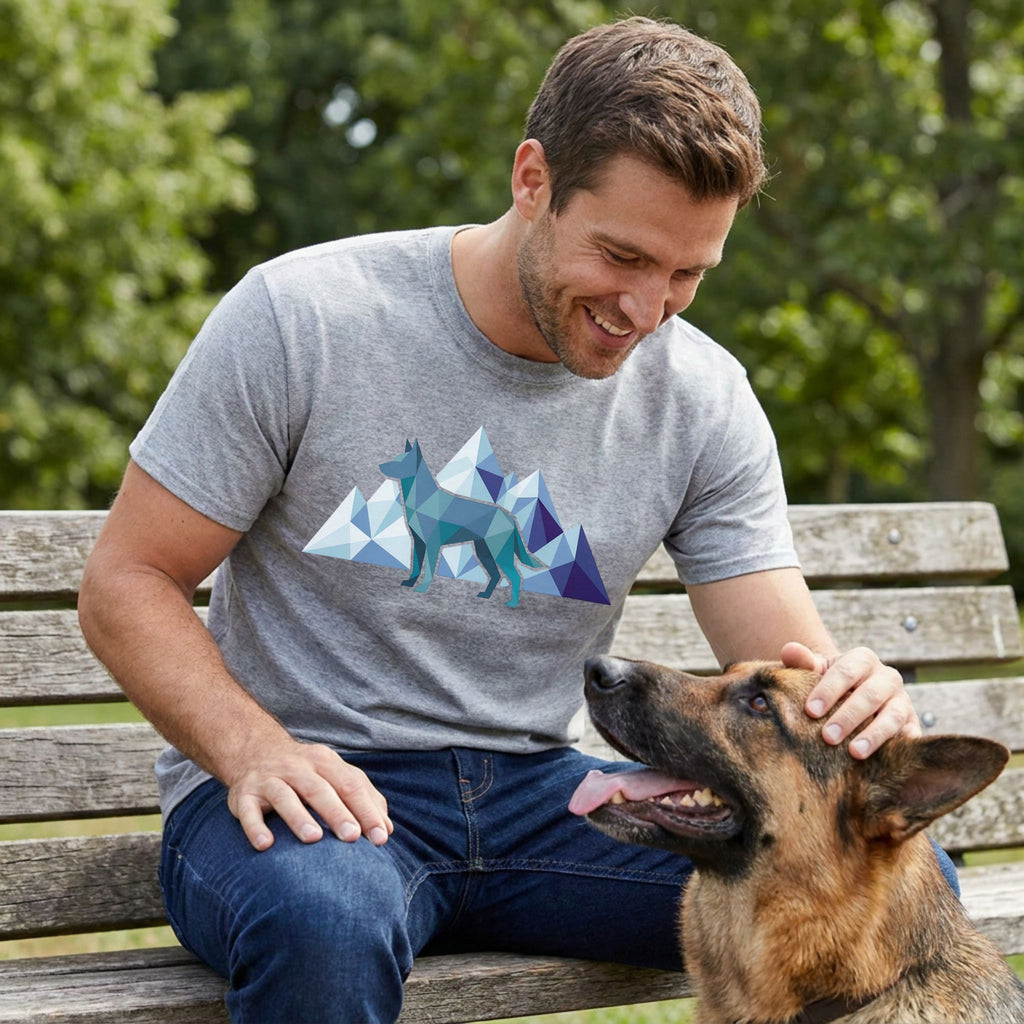 Man in a grey "Canine Explorer" t-shirt with geometric dog and mountains, petting a German Shepherd.