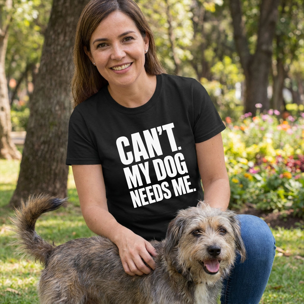 Woman wearing a black crew neck t-shirt with white CAN'T. MY DOG NEEDS ME. text, kneeling outdoors with a scruffy dog.