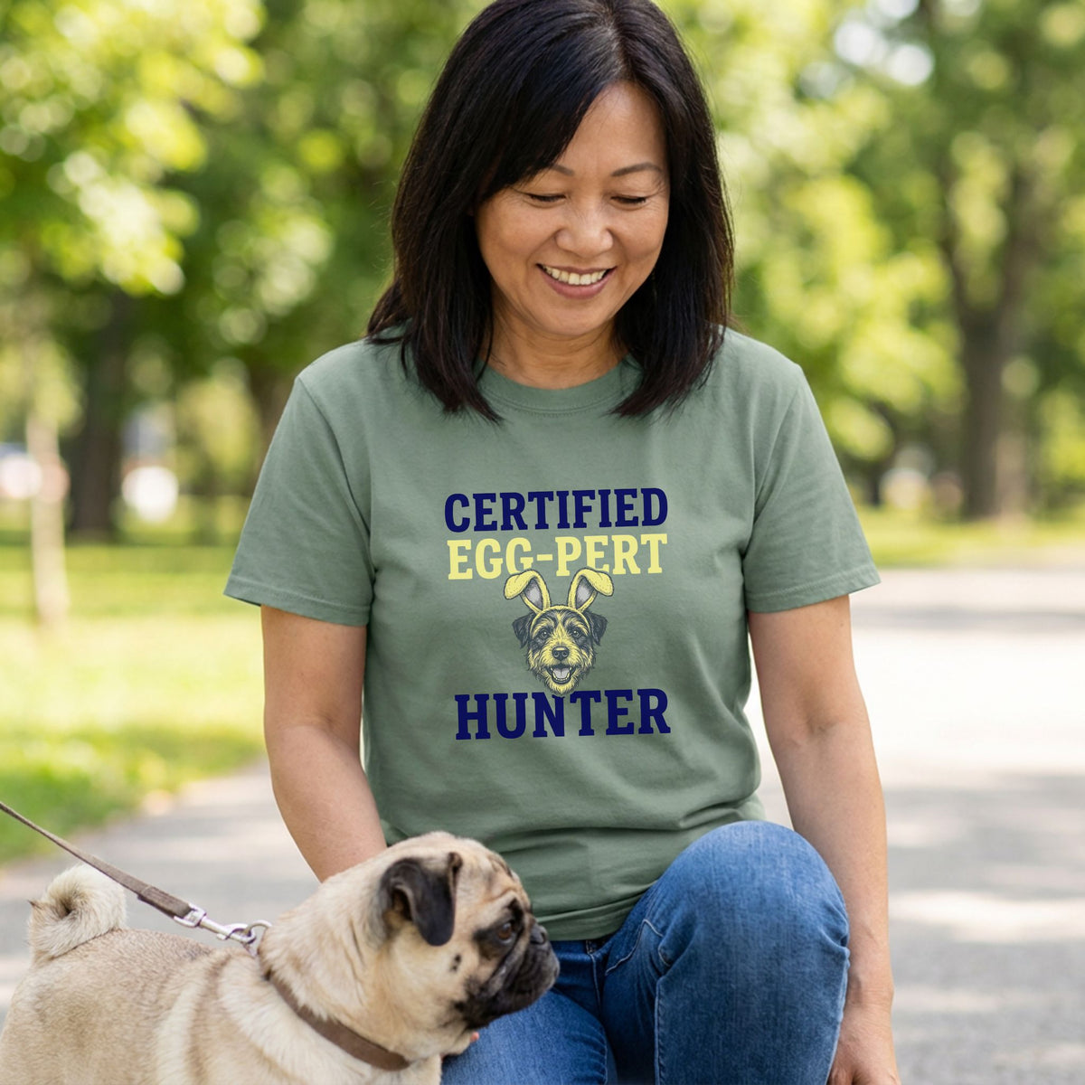 Woman in a green "Certified Egg-Pert Hunter" t-shirt with a dog wearing bunny ears, next to a pug.