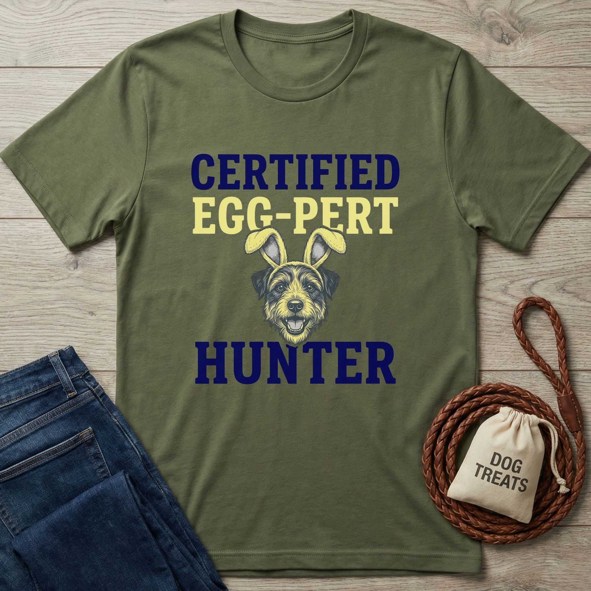 Olive green "Certified Egg-Pert Hunter" t-shirt with a dog wearing bunny ears, beside jeans and dog treats.