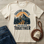Cream-colored graphic t-shirt featuring a hiker and dog on a mountain trail with the text Chasing Summits.