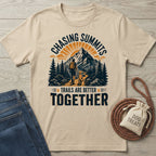 Beige crewneck t-shirt featuring a graphic of a hiker and dog on a mountain trail with the text Chasing Summits.