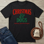 Black cotton T-shirt with vintage red and green Christmas and Dogs holiday graphic text on a wooden background.