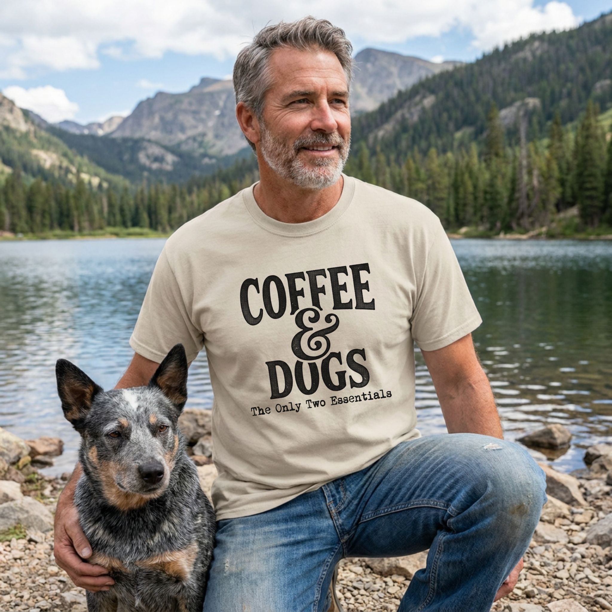 Man in a tan "Coffee & Dogs" t-shirt with a blue heeler dog by a mountain lake.