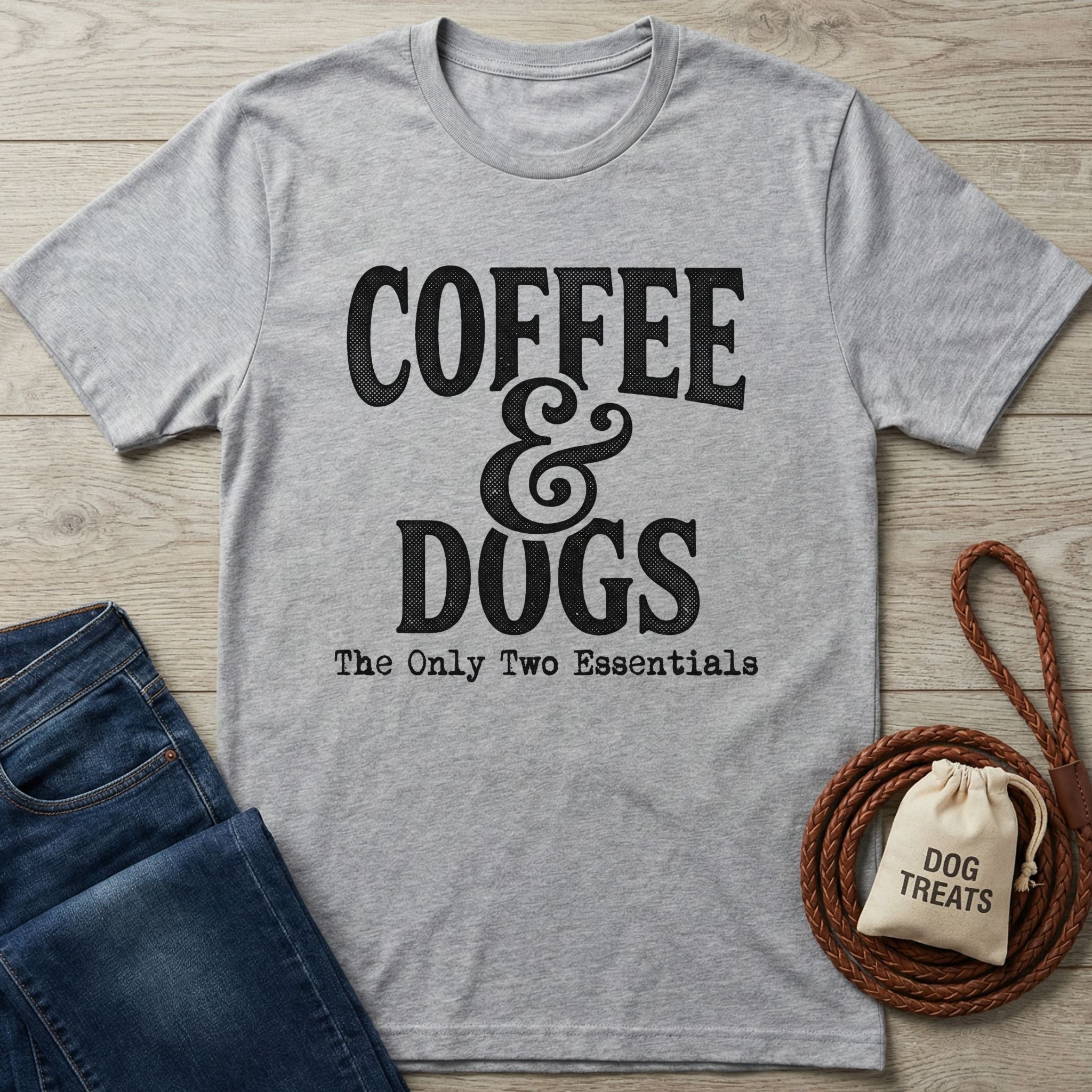 Light grey Gildan Softstyle® t-shirt with "Coffee & Dogs The Only Two Essentials" text, beside jeans and dog treats.