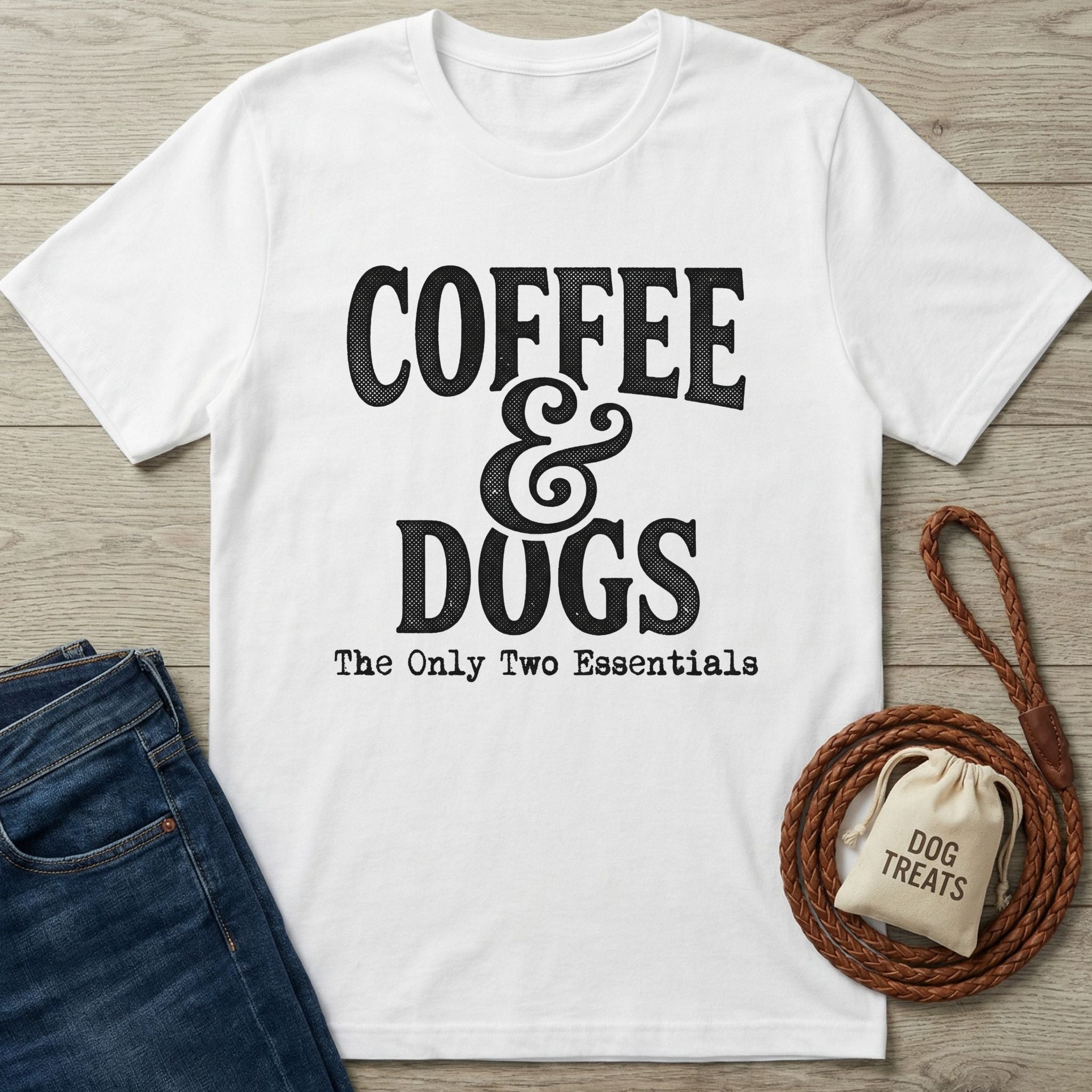 White Gildan Softstyle t-shirt with "Coffee & Dogs: The Only Two Essentials" in black text, next to jeans and a leash.