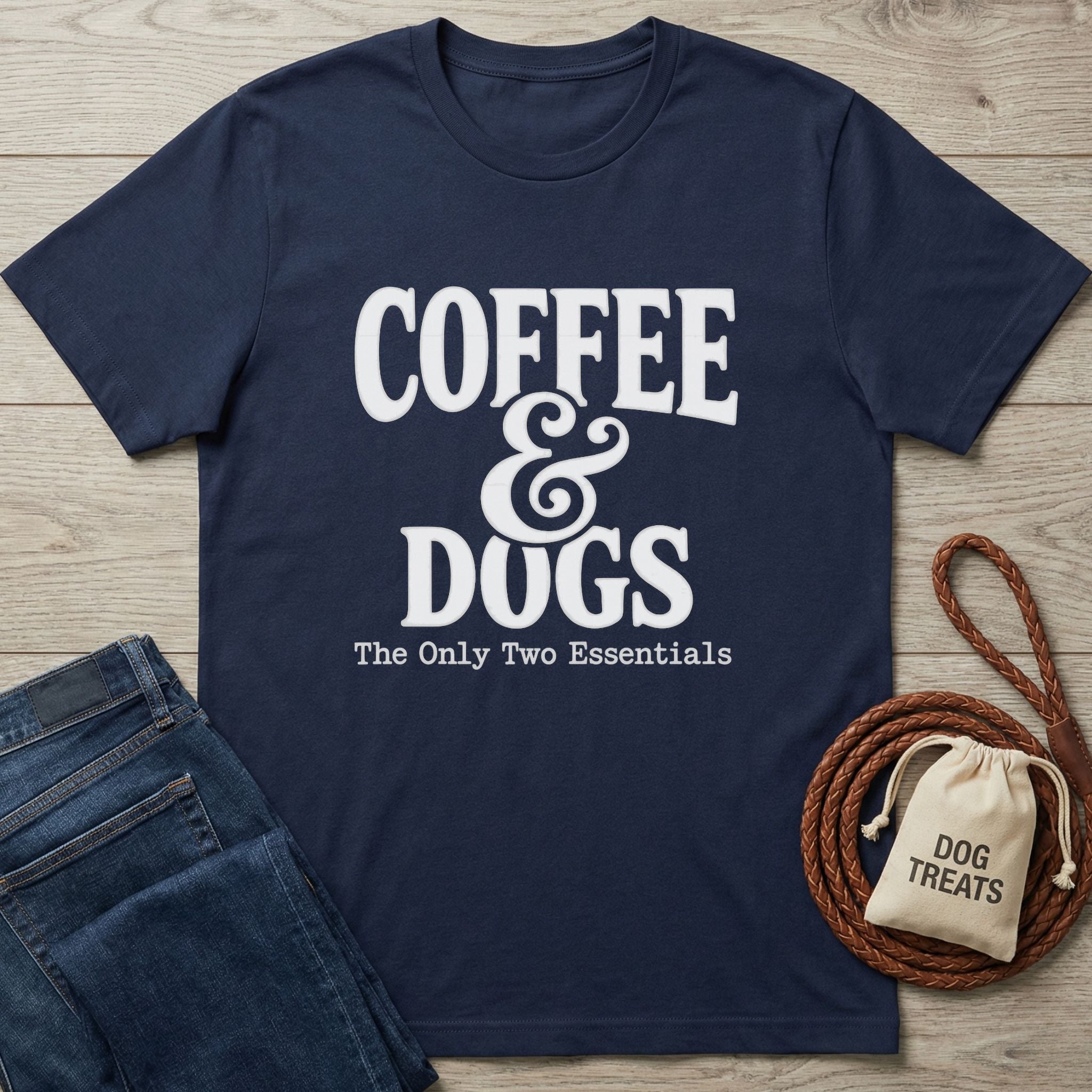 Navy blue Gildan Softstyle® t-shirt with "Coffee & Dogs The Only Two Essentials" in white text, next to jeans and dog treats.