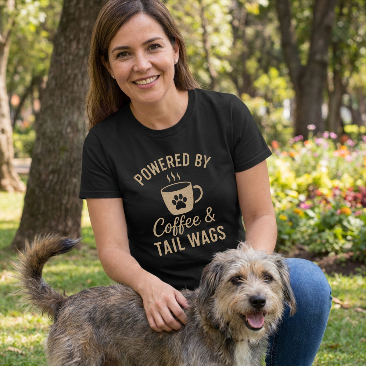 Woman in black "Powered by Coffee & Tail Wags" t-shirt, petting a scruffy dog outdoors.