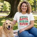 Woman wearing a white crewneck T-shirt with red and green festive text sitting in a park with a golden retriever.