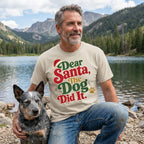 Man wearing a beige t-shirt with festive red, green, and gold Dear Santa, The Dog Did It text by a lake.