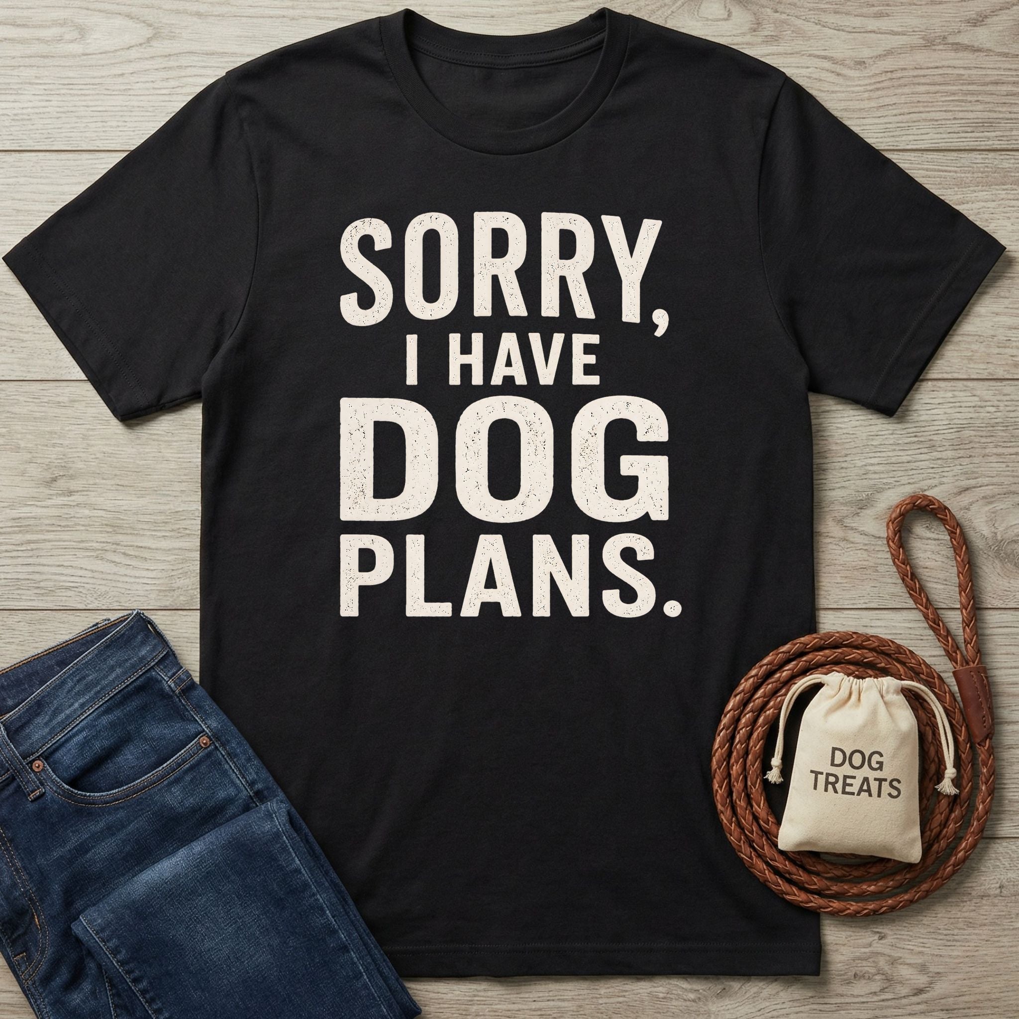 Black crewneck t-shirt with white distressed text reading Sorry, I Have Dog Plans, laid on a wooden surface with jeans and a leash.