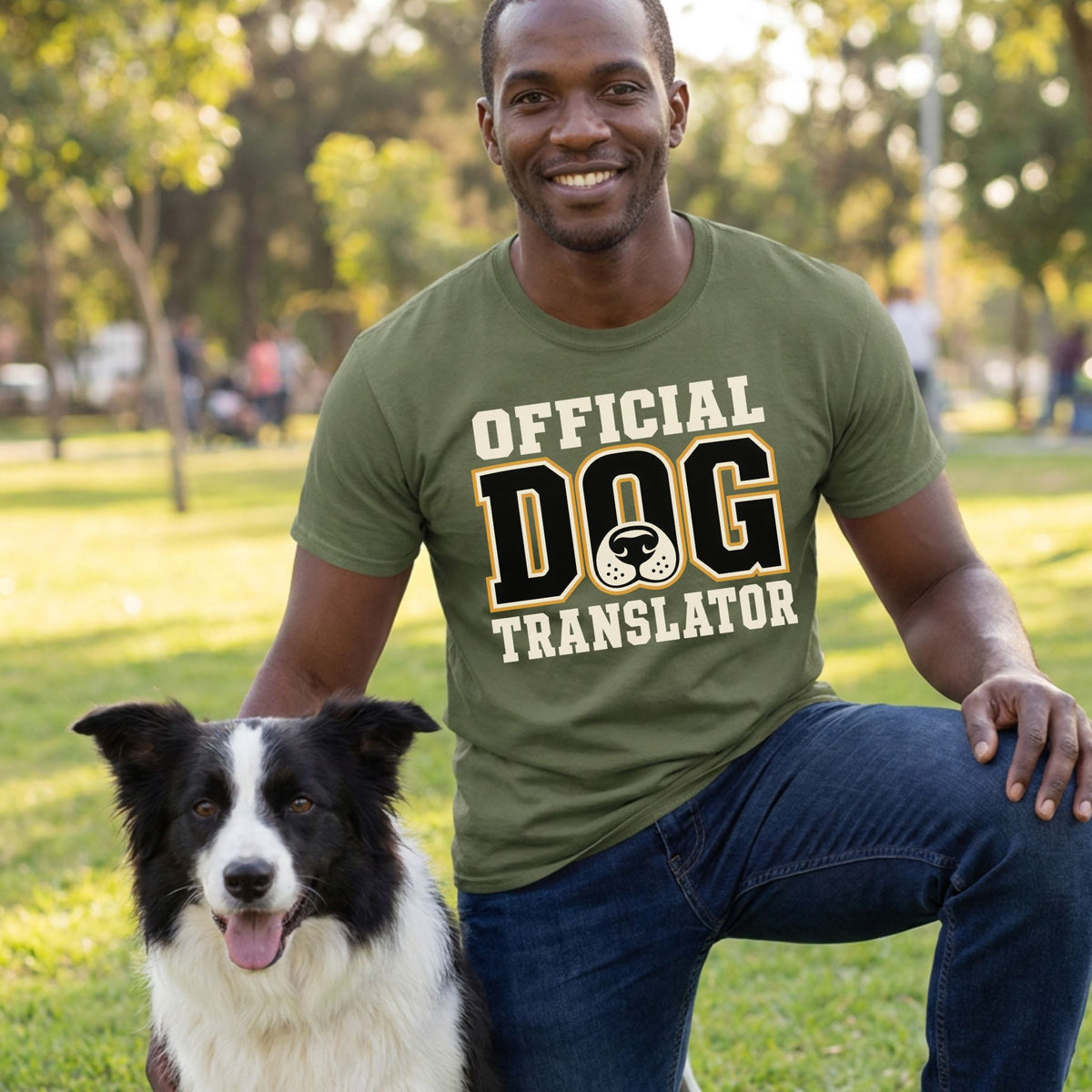 Man wearing an olive green crewneck t-shirt with Official Dog Translator text and a dog nose graphic, kneeling with a dog.