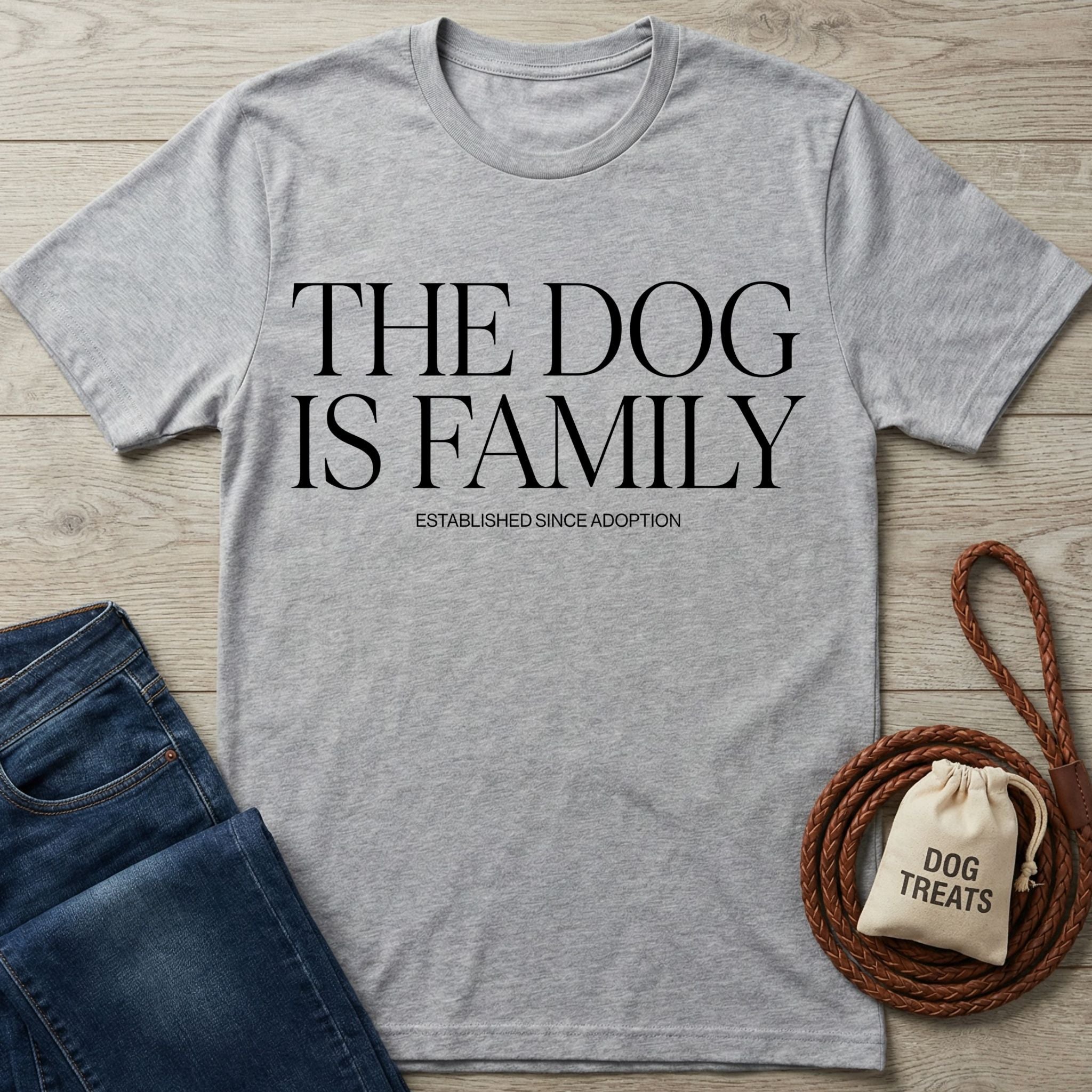 Light grey Gildan Softstyle® t-shirt with "THE DOG IS FAMILY" text, next to jeans and dog treats.