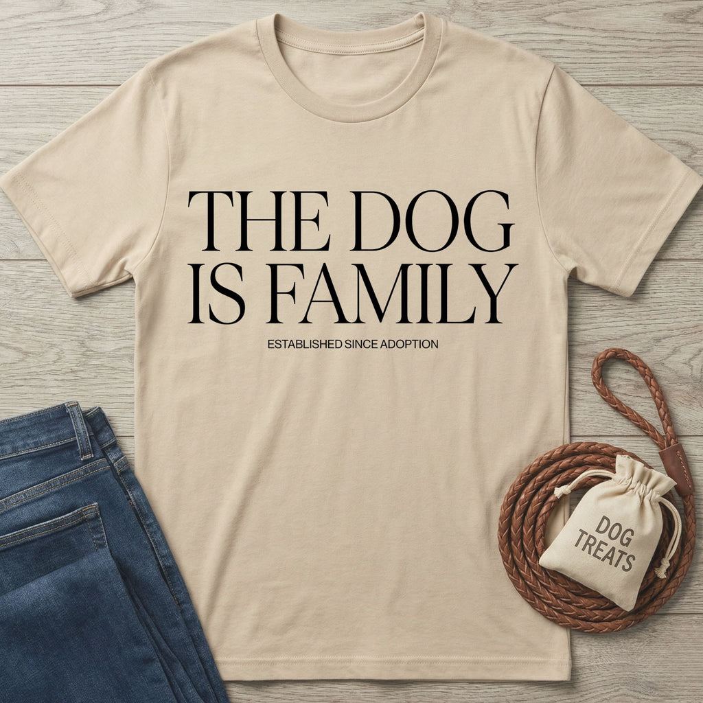 Beige Gildan Softstyle® t-shirt with "THE DOG IS FAMILY" text, next to jeans and dog treats.