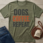Olive green crewneck t-shirt featuring the text Dogs, Coffee, Repeat in black and orange, laid out with jeans and a dog leash.