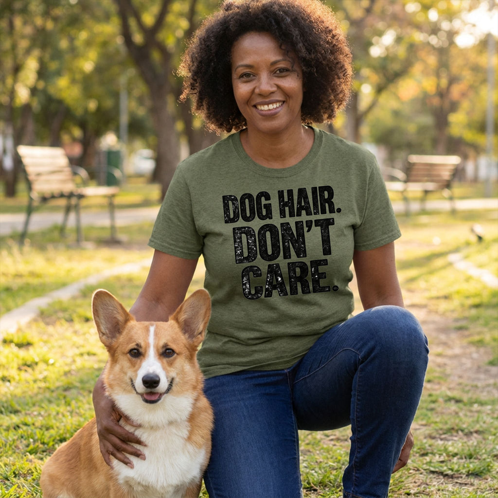 Woman wearing an olive green crewneck t-shirt with distressed black text reading Dog Hair. Don't Care. while kneeling with a corgi.