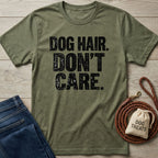 Olive green crewneck t-shirt with distressed black text reading DOG HAIR. DON'T CARE. on a wooden background with dog accessories.