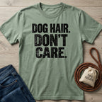 Sage green crewneck t-shirt with distressed black text reading DOG HAIR. DON'T CARE. laid on a wooden surface with a leash.