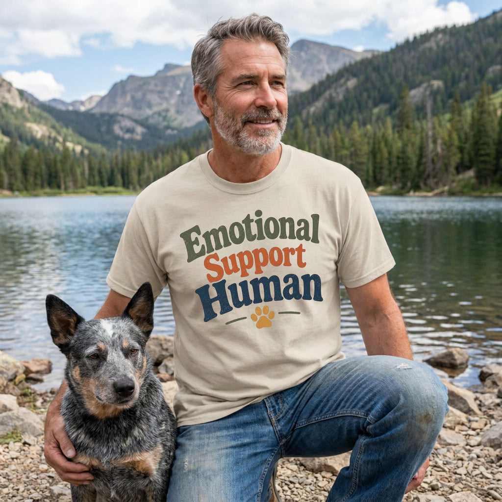 Beige "Emotional Support Human" t-shirt on a man with a dog by a lake.