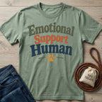 Sage green "Emotional Support Human" t-shirt with a paw print, next to blue jeans, a leash, and a "Dog Treats" bag.