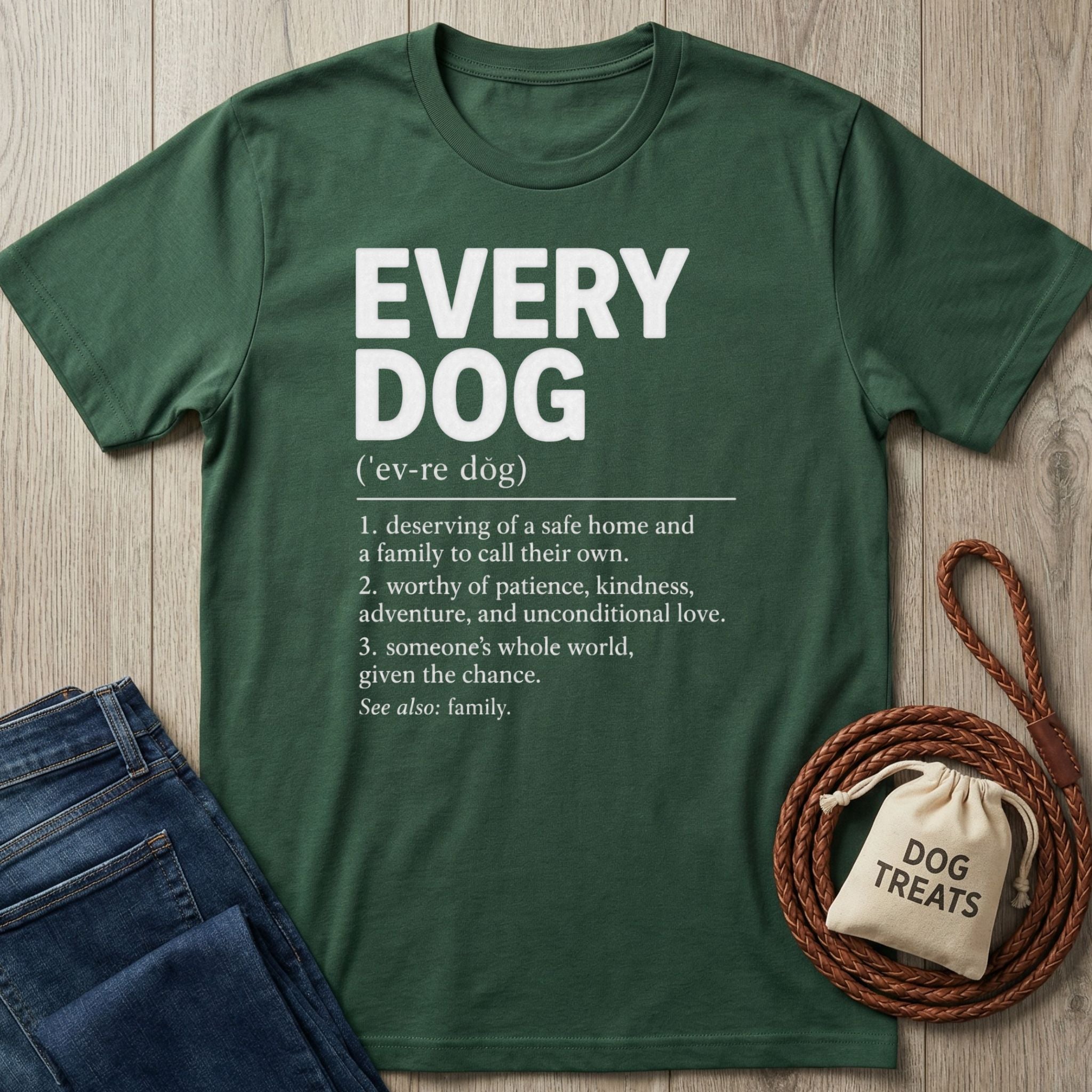 Forest green cotton t-shirt featuring a white dictionary-style definition of Every Dog, laid flat with a leash and treat bag.