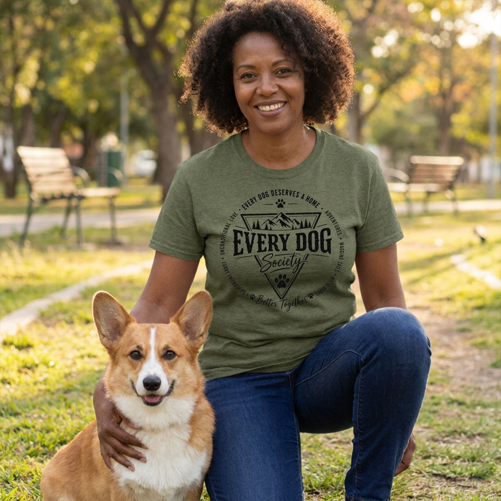 Woman wearing an olive green Every Dog Society graphic t-shirt while kneeling next to a Corgi in a park.