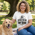 Woman wearing a white crew neck t-shirt with a dog graphic, sitting on a blanket in a park next to a golden retriever.