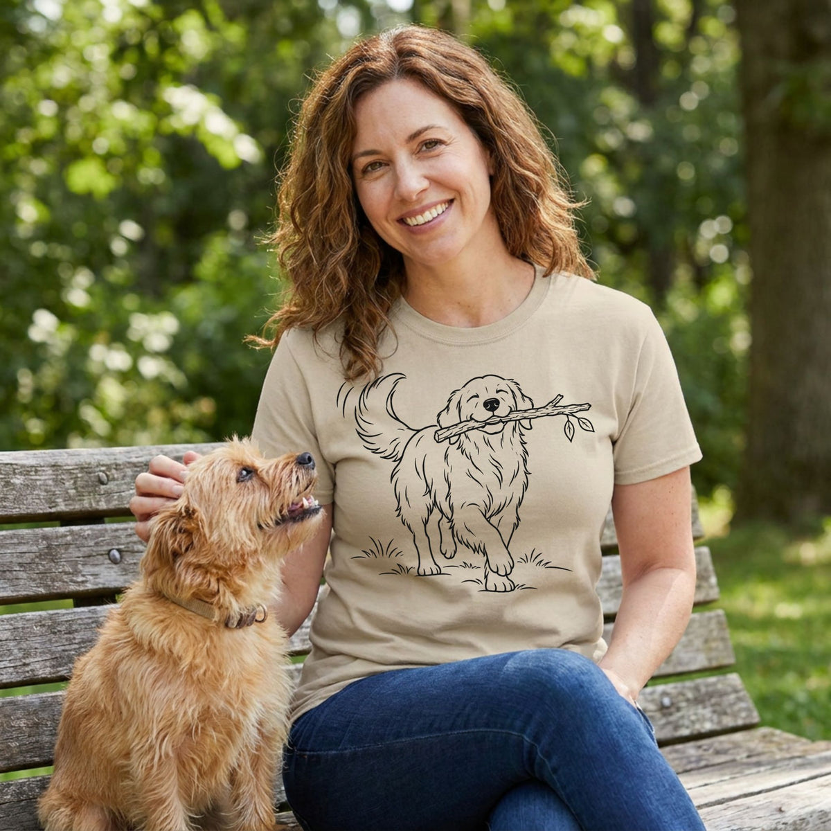 Woman wearing a beige crewneck t-shirt with a black line art illustration of a dog carrying a stick, sitting on a park bench.