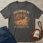 Charcoal grey cotton T-shirt featuring a vintage beach graphic with human footprints, paw prints, and the text Followed By Love.