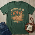 Forest green cotton T-shirt featuring a beach graphic with human footprints and dog paw prints, text reads Followed By Love.
