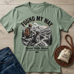 Sage green "Found My Way" t-shirt with a graphic of a person and dog on a mountain trail.