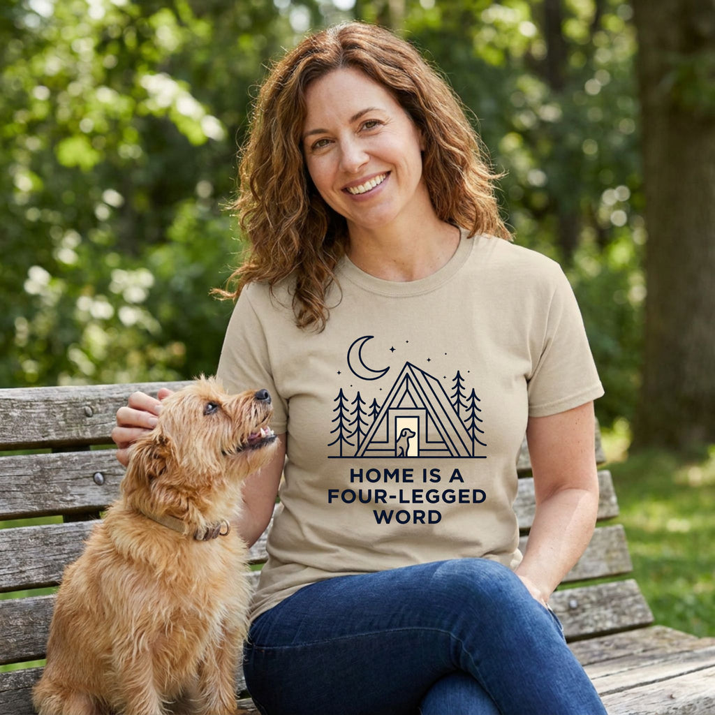 Smiling woman in a tan "Home is a Four-Legged Word" graphic tee petting a small dog on a park bench.