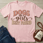 Light pink crew neck T-shirt with retro brown text reading Dogs Are A Girl's Best Friend, laid on a wooden surface.