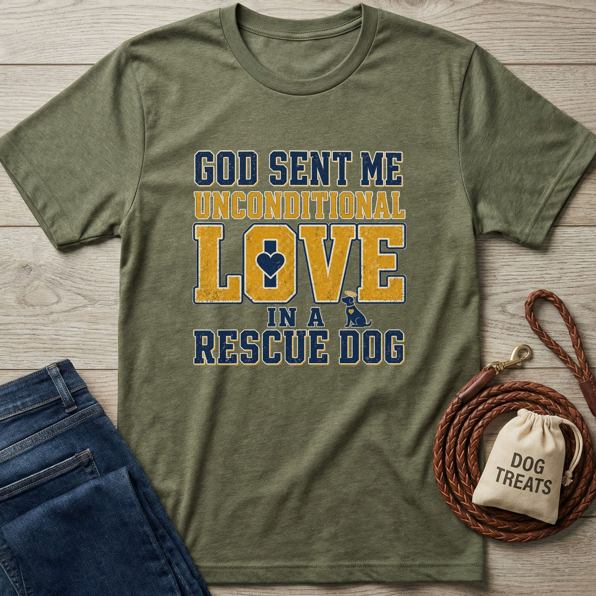 Olive green "God Sent Me Unconditional Love In A Rescue Dog" tee with blue and gold distressed text, beside jeans and dog accessories.