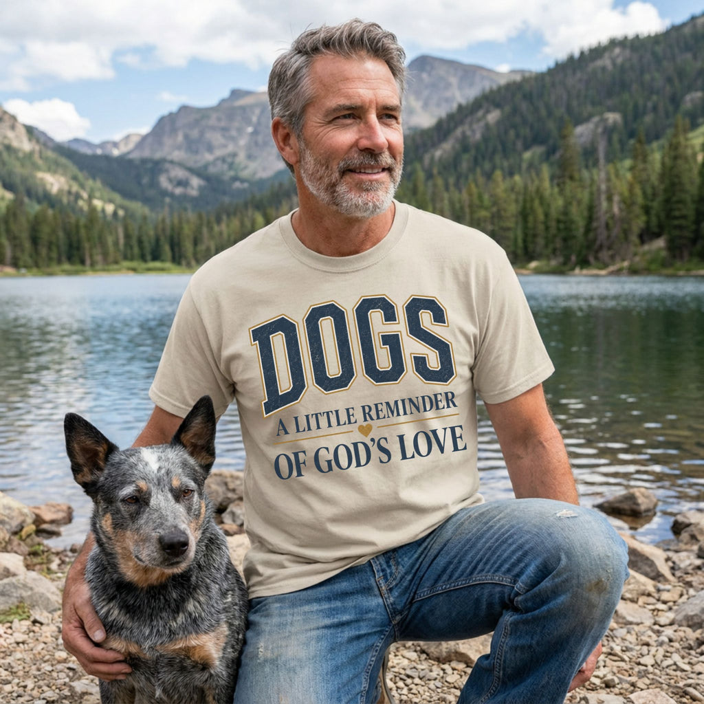 Man wearing a beige crewneck t-shirt with Dogs A Little Reminder Of God's Love text, posing with a dog by a mountain lake.