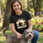 Woman in black Golden Souls T-shirt with sunset design, petting a senior dog in a park.