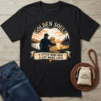 Black cotton t-shirt with "Golden Souls" sunset graphic of a person and senior dog by a lake.